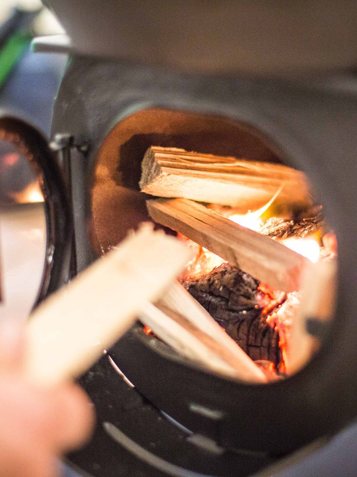 Anevay Frontier Plus lit with kindling being fed into the fire - Outdoor Wood Burning Stove