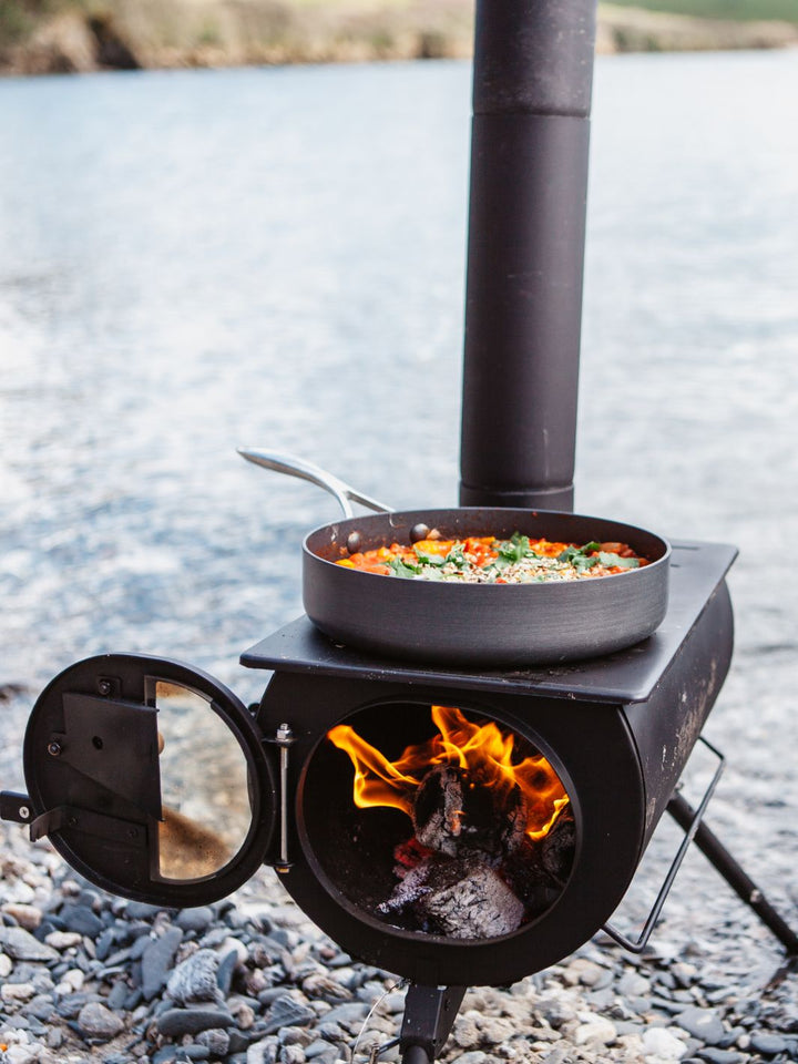 Anevay Frontier Plus set up on a shingle beach with food cooking on top  - Outdoor Wood Burning Stove
